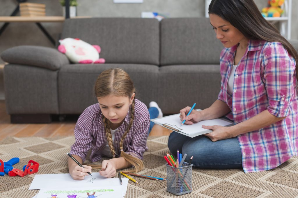 female ABA therapist taking notes while girl drawing white paper